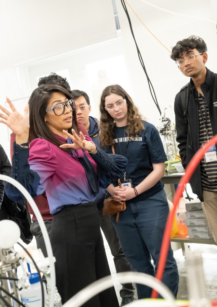 An instructor gestures while explaining lab equipment to a group of students during a hands-on entrepreneurship lab tour at the University of Michigan.